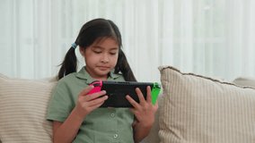 Happy Asian young girl using a tablet while sitting on a couch, child holding console playing video game on sofa in living room at home, technology online game concept - Powered by Shutterstock - Get 15% off with code: PIKWIZARD15