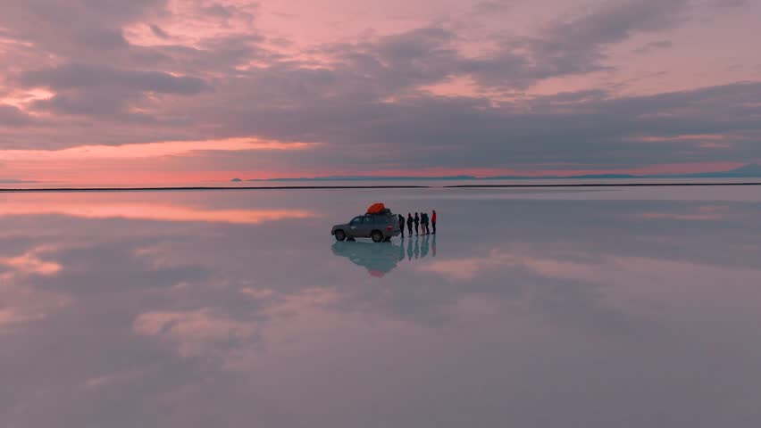 Sunrise Over Salar de Uyuni with Reflections and Group of People Standing in Shallow Water. A breathtaking red-pink sunrise over the Salar de Uyuni salt flats in Bolivia