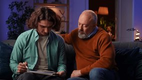 An elderly man learns how to draw on a graphics tablet and a young man controls the process using a laptop. Grandson teaches grandfather how to design while sitting at home in the evening. - Powered by Shutterstock - Get 15% off with code: PIKWIZARD15