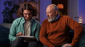 An elderly man learns how to draw on a graphics tablet and a young man controls the process using a laptop. Grandson teaches grandfather how to design while sitting at home in the evening. - Powered by Shutterstock - Get 15% off with code: PIKWIZARD15