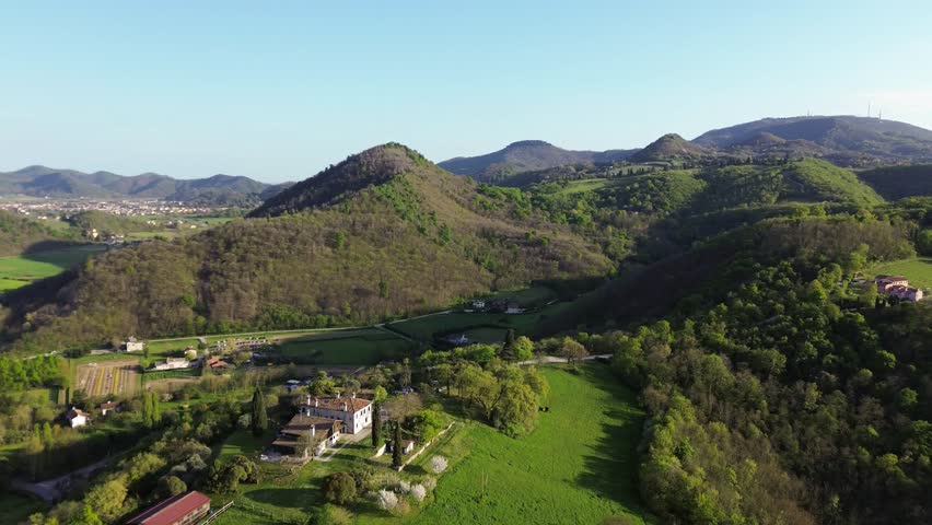 Panning aerial view of an old house in a green landscape with Monte Venda mountain in Colli Euganei hills with setting sun casting warm light on the hillside