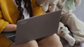 Tilt up shot of single Asian mother working on laptop sitting next to little daughter playing toys at home - Powered by Shutterstock - Get 15% off with code: PIKWIZARD15