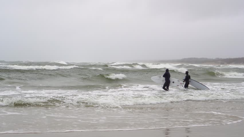 Two surfer in wetsuit trying to catch a wave in a cold stormy sea on a windy day. Extreme sport experience, life full of adrenaline and challenges.