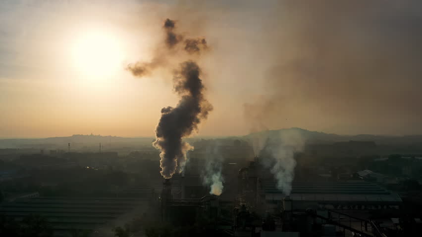 Aerial footage shows smoke rising from industrial plants, highlighting the scale of manufacturing and its environmental impact. The scene captures the powerful energy of modern industry.
