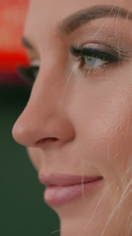 Cheerful blonde woman with glamorous makeup smiles standing on blurred background with blinking lights extreme close side view slow motion