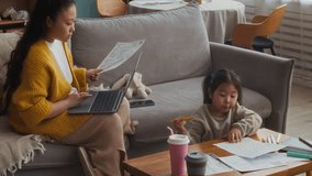Medium long shot of Asian mother paying bills online on laptop while her daughter drawing on paper and drinking at home - Powered by Shutterstock - Get 15% off with code: PIKWIZARD15