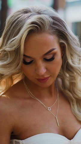 Attractive lady bride with long curly hair in white wedding dress waves skirt train standing in green sunny city park close view slow motion