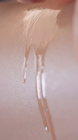 Young woman makes massage of back spreading liquid aroma oil on soft skin in circular motion with fingers skincare routine closeup slow motion