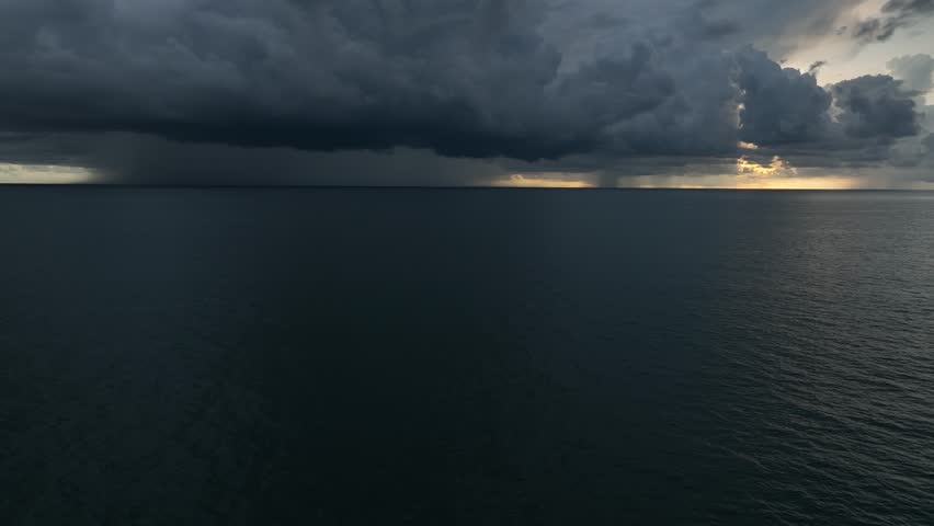 Captured from the sky, dark clouds loom over the ocean, as the storm builds in intensity, with rainfall starting to blur the horizon, signaling an impending downpour.
