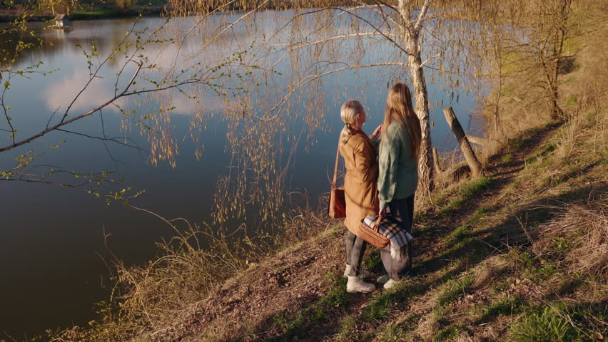 Middle-aged woman and teenage girl standing near a birch tree by the river, closely observing the spring buds during a peaceful nature walk. High quality 4k footage