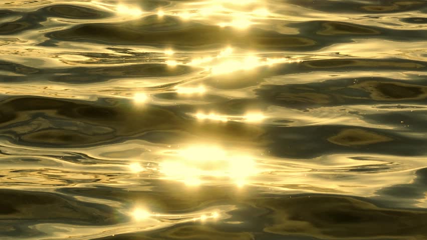 The drone captures the shimmering surface of the water, reflecting golden light as the sun dances across the rippling waves, creating a mesmerizing and tranquil scene.
