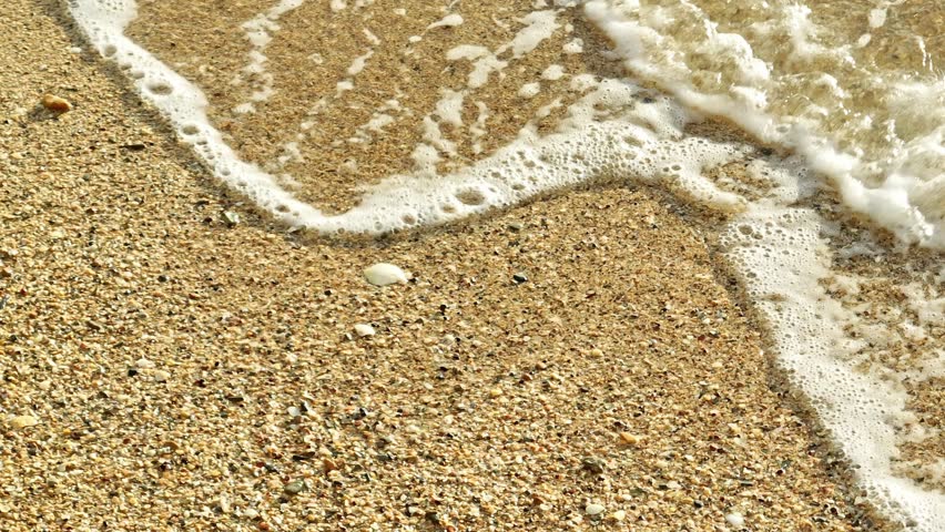 Captured in slow motion, the water rushes to the shore, its foamy edges blending with the grains of sand, highlighting the ocean