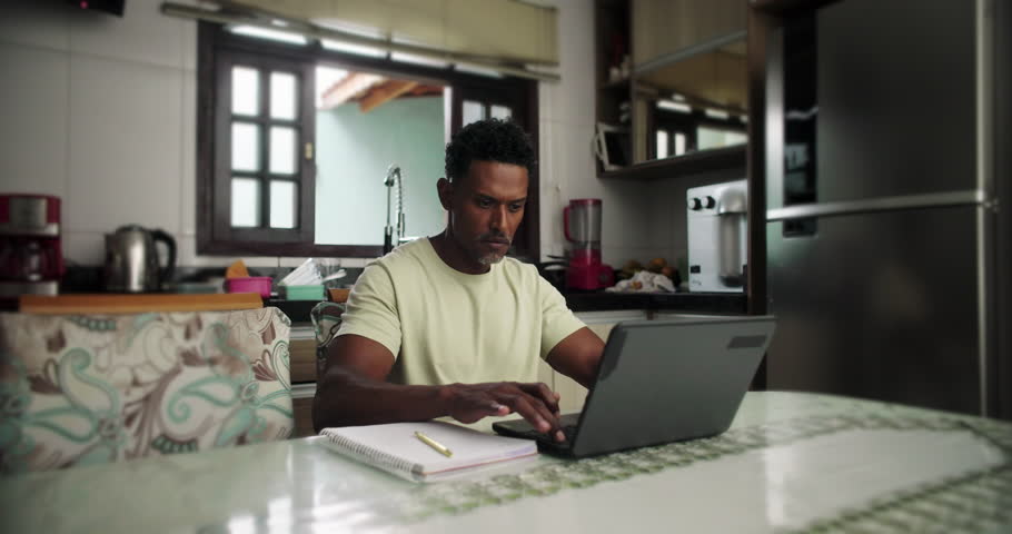 Man working on laptop with hand on chin, deep thought, problem-solving, remote work, home office, focus, serious expression, concentration, professional workspace