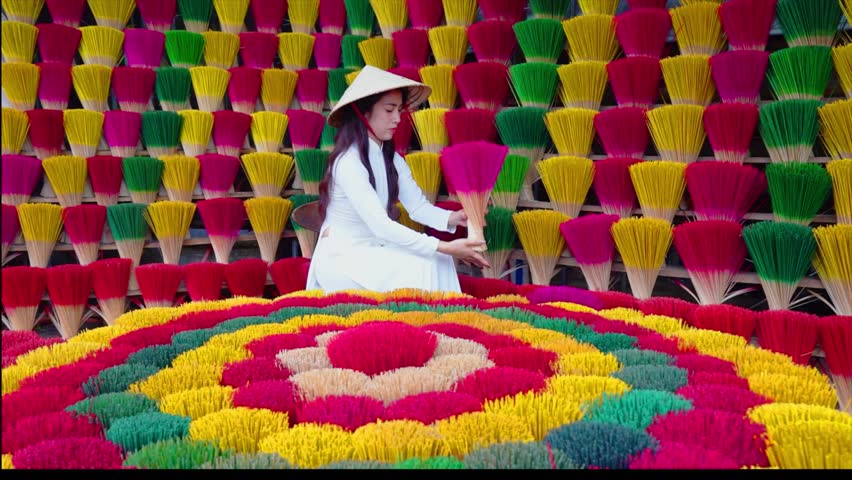A young Vietnamese woman in a white national costume arranges colorful incense sticks in Hue, Vietnam.