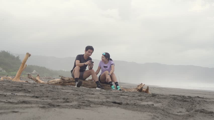active young asian couple resting and chatting after running exercise on the beach