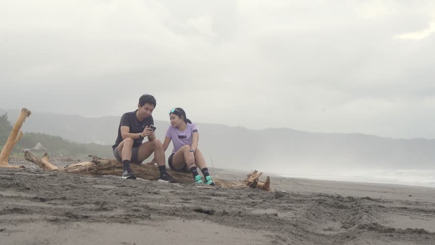 active young asian couple resting and chatting after running exercise on the beach