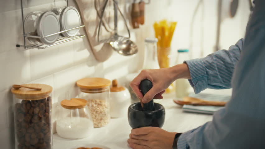 An individual is grinding spices in a mortar and pestle in a contemporary kitchen