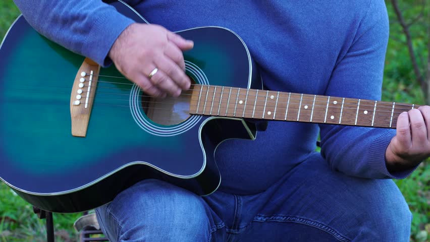 Man plays guitar outdoors at the backyard
