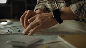 Hands are organizing a detailed map on a table, using blue push pins for navigation. The activity takes place indoors, focusing on planning a trip or adventure - Powered by Shutterstock - Get 15% off with code: PIKWIZARD15