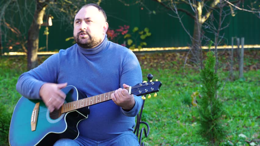 Man plays guitar outdoors at the backyard
