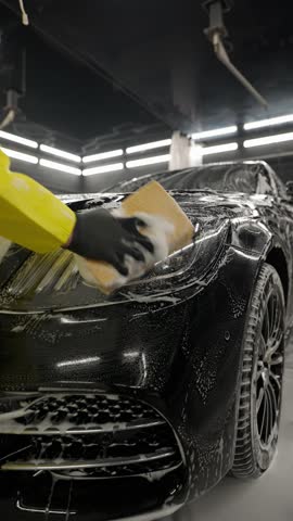 Worker washes car with sponge, detailed cleaning process in modern car wash center.