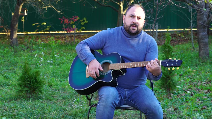 Man plays guitar outdoors at the backyard
