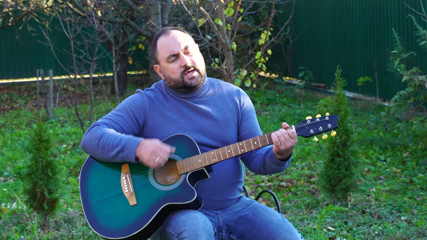 Man plays guitar outdoors at the backyard
