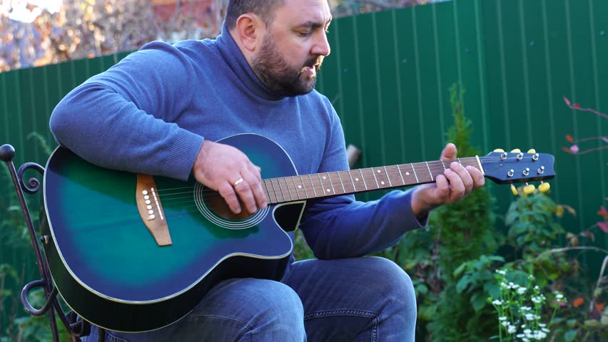 Man plays guitar outdoors at the backyard
