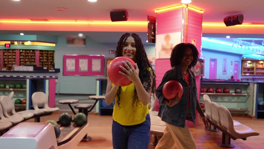 Young woman throwing bowling ball, knocking down pins in perfect strike while celebrating with enthusiastic joy and excitement in brightly lit bowling alley during weekend leisure activity