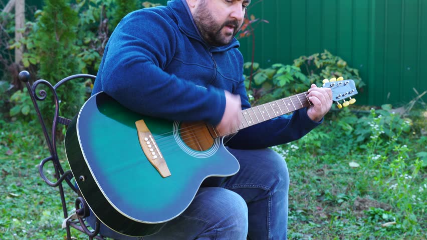 Man plays guitar outdoors at the backyard
