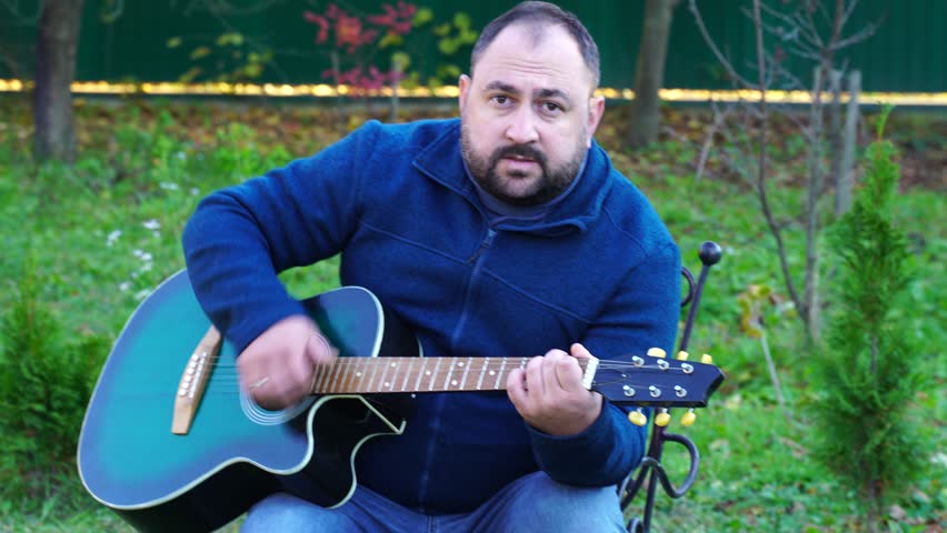 Man plays guitar outdoors at the backyard
