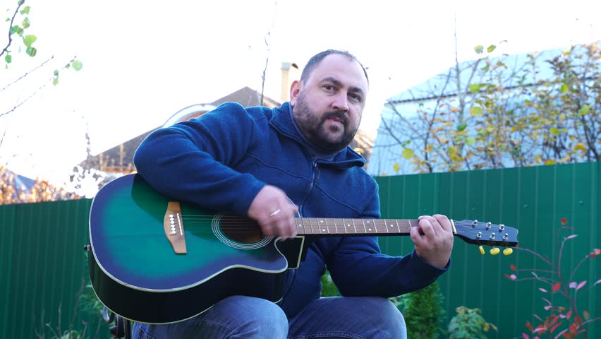 Man plays guitar outdoors at the backyard
