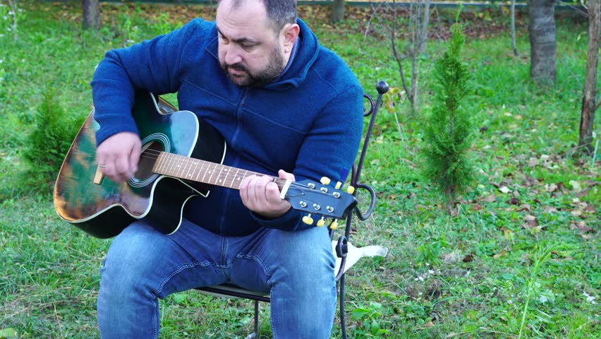 Man plays guitar outdoors at the backyard
