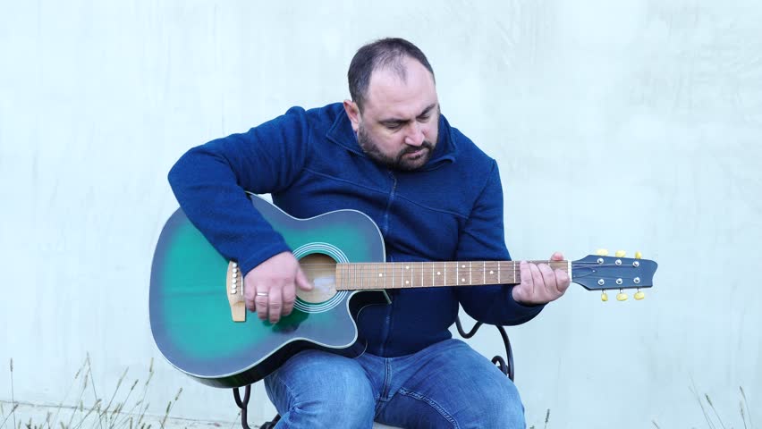 Man plays guitar outdoors at the backyard
