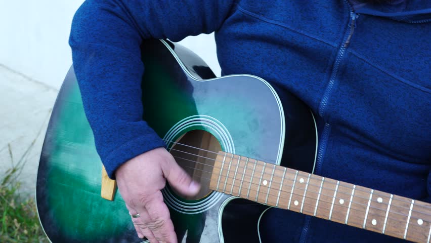 Man plays guitar outdoors at the backyard
