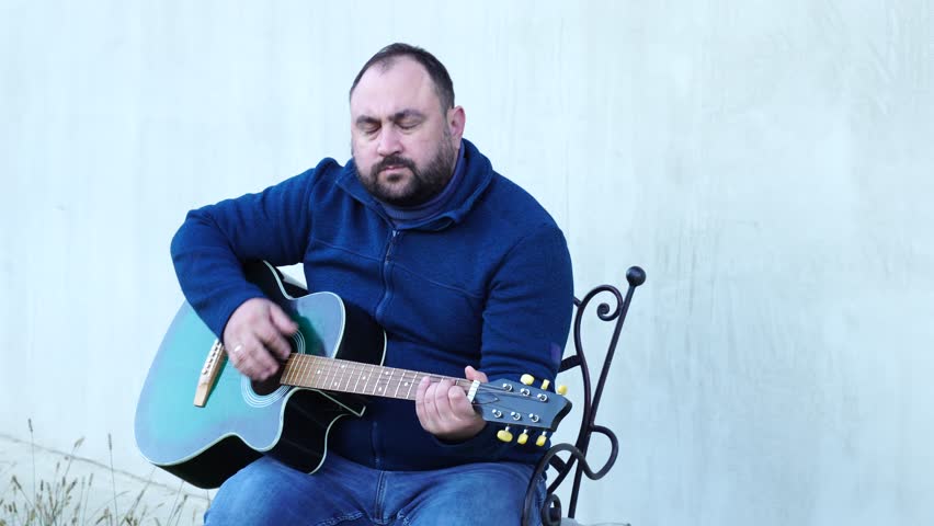 Man plays guitar outdoors at the backyard

