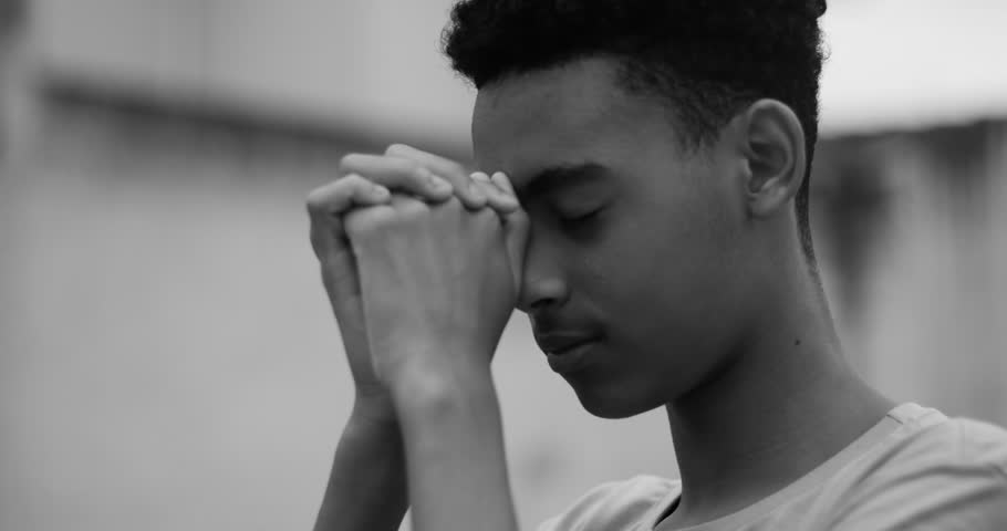 Teenage boy with hands clasped, eyes closed, deep in prayer, peaceful expression, moment of faith, spirituality, devotion, gratitude, personal connection, emotional reflection