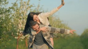 Cheerful young woman riding piggyback on her boyfriend in a beautiful orchard, surrounded by fresh green grass and blossoming trees under warm spring sunshine. - Powered by Shutterstock - Get 15% off with code: PIKWIZARD15