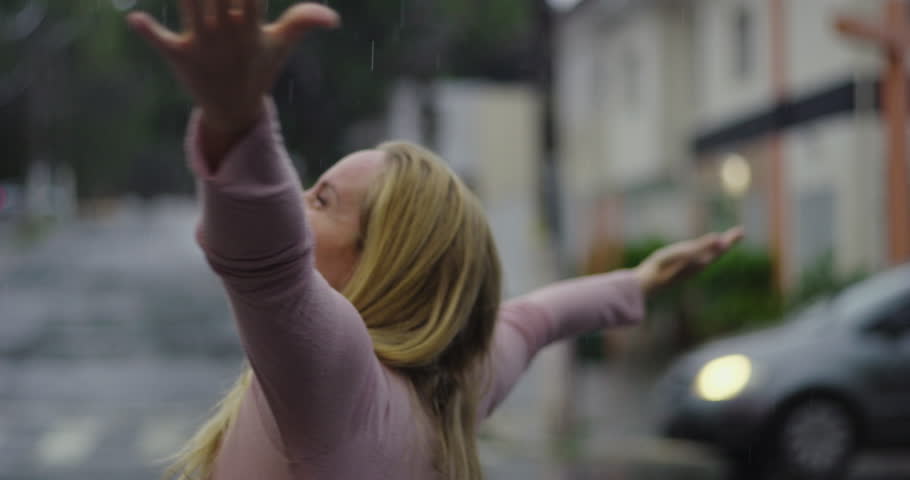 Woman embracing rain with joyful smile, arms wide open, head tilted back in moment of freedom and emotional release