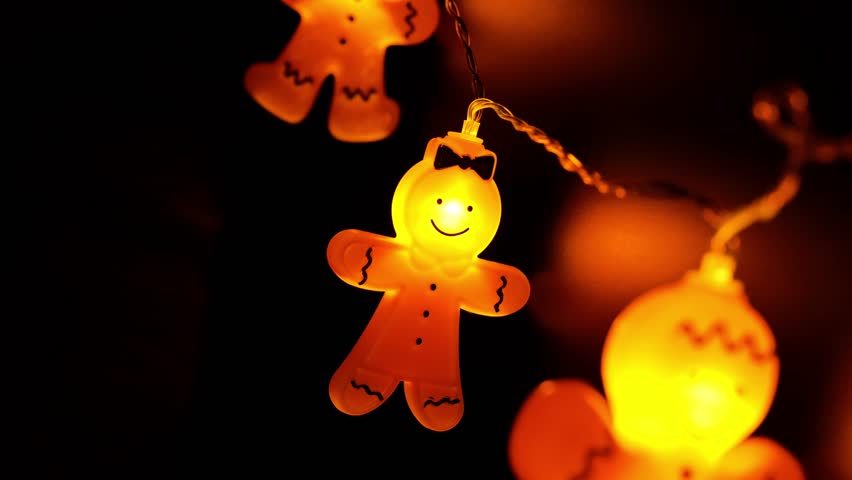 Gingerbread men row on black background. Glowing Christmas garland in the dark. Warm light Christmas garland. 4k footage