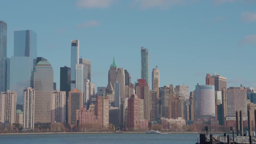 A wide shot of Lower Manhattan’s skyline viewed from across the Hudson River on a clear day, featuring iconic high-rises and a passing ferry.