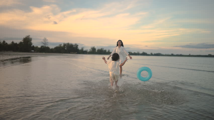 Child runs into mother's arms in shallow sea under glowing sunset sky, capturing movement, trust, deep emotional connection, and unconditional love in soft natural light.