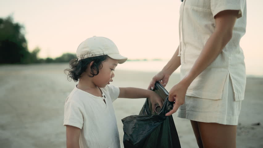 Child holds out trash to mother during beach cleanup, showing care, focus, and early responsibility through a simple, meaningful act in soft natural light by the sea.