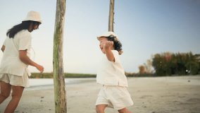 Child playfully chases mother on quiet beach during golden hour, expressing freedom, laughter, and emotional bonding through natural movement in warm, soft evening light. - Powered by Shutterstock - Get 15% off with code: PIKWIZARD15