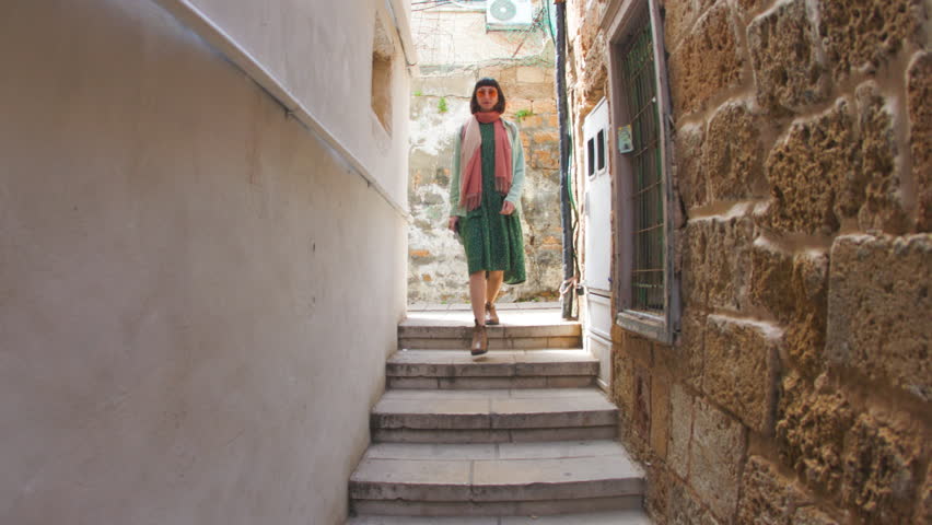 girl confidently walks along the street of the old city. Young attractive tourist with a backpack wanders along the street of the old city during a trip, admiring the architecture, looking around. 