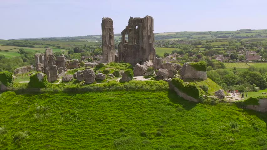 Slow motion drone footage of Corfe Castle’s weathered stone ruins set against the rolling green countryside and village landscape in Dorset, England