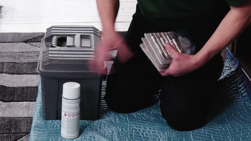 Worker packs toolbox on floor, lifts it and exits home frame in single take