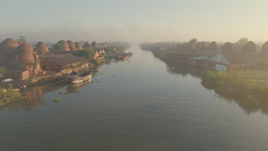 Brick making Kiln lined along river in Mekong Delta . Drone fly through during soft early morning light. Vinh Long, Vietnam.