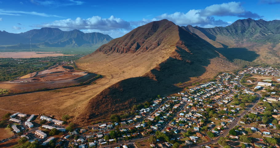 Approaching a spectacular bare rocks with rugged slopes. Residential area with multiple houses scattered at the foot of the mountains. Aerial view.