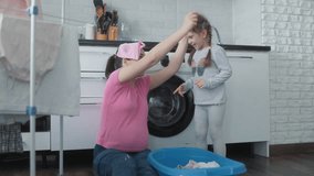 In a bright kitchen, a mother playfully interacts with her young daughter as they sort laundry together. The cozy atmosphere highlights their bonding time during house chores. - Powered by Shutterstock - Get 15% off with code: PIKWIZARD15